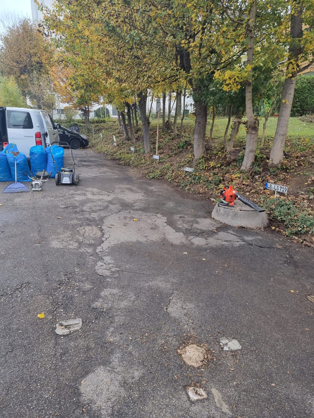 Laubräumung auf einer Hoffläche im Herbst mit Laubbläser, Kehrmaschine und gefüllten Laubsäcken