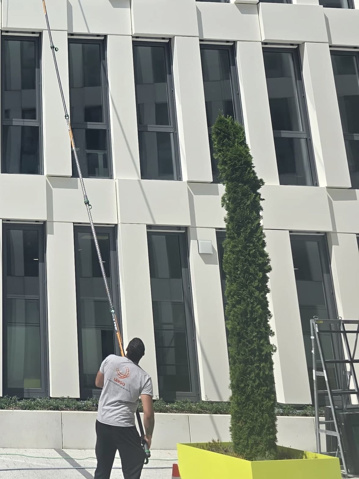 Largo-Mitarbeiter reinigt die Fenster einer weißen Bürofassade mit der Osmose-Teleskopstange