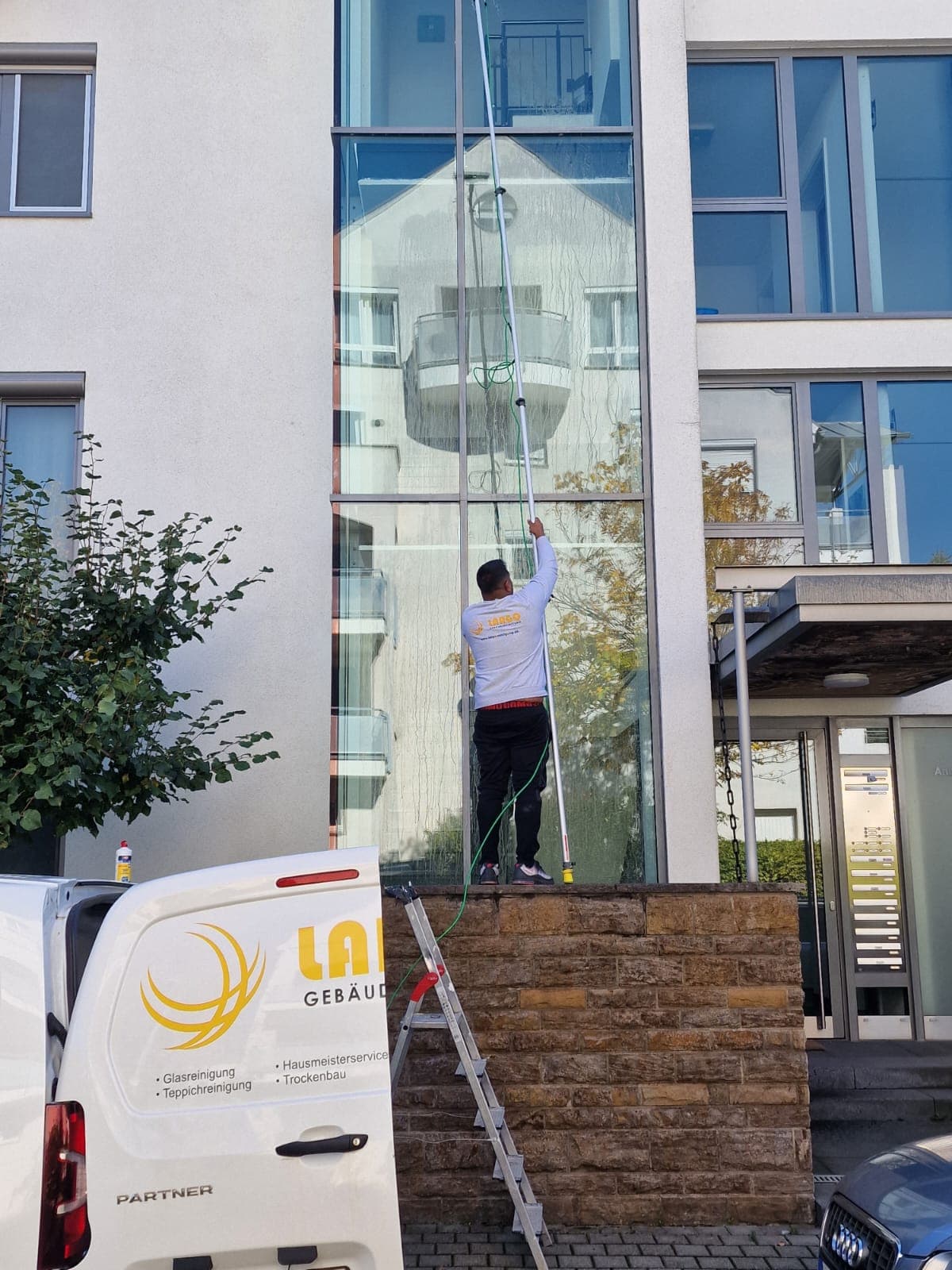 Largo-Mitarbeiter reinigt eine Glasfassade in Leonberg mit der Osmose-Teleskopstange, daneben der beschriftete Firmentransporter